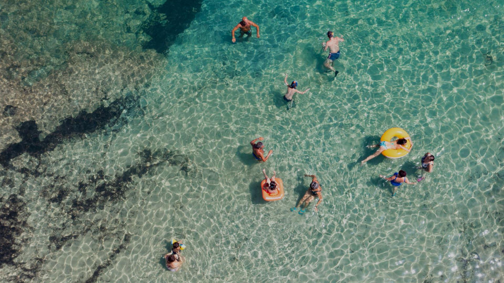 Persone nuotano e si divertono in acque cristalline con ciambelle galleggianti.