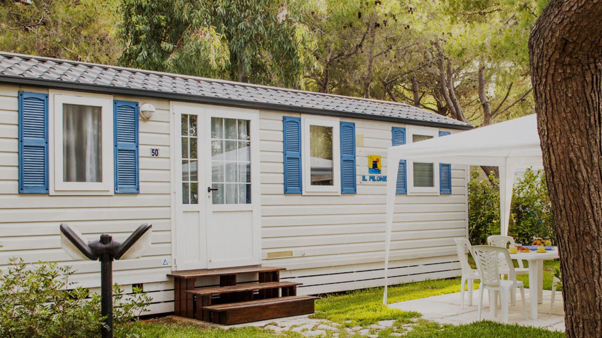 Casa mobile con veranda in un campeggio circondato da alberi.