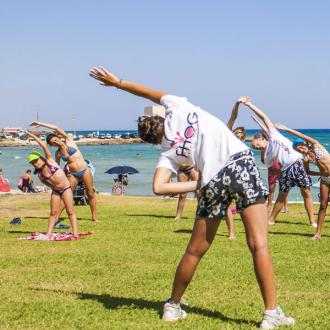 Gruppo di persone fa stretching sulla spiaggia in una giornata soleggiata.