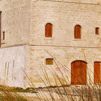 Antica torre in pietra vicino al mare, con finestre ad arco e porte in legno.