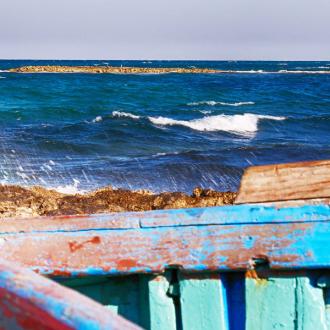 Barca di legno colorata sulla riva con mare mosso sullo sfondo.