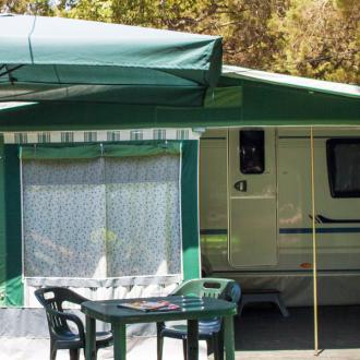 Roulotte con veranda verde, tavolo e sedie all'aperto, ombrellone sopra.