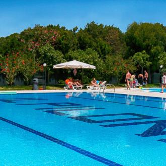 Piscina all'aperto con lettini, ombrelloni e persone che si rilassano.