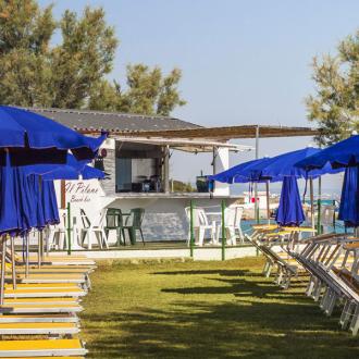 Spiaggia con ombrelloni blu, lettini e bar vicino al mare.
