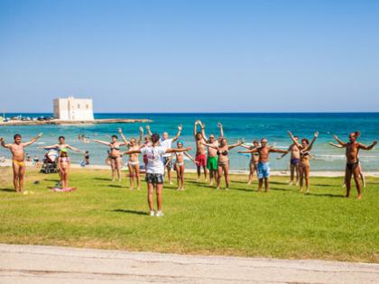 Persone fanno esercizi in gruppo su un prato vicino al mare.