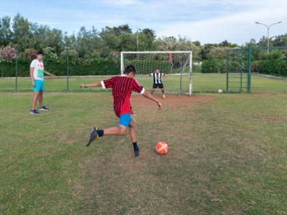 Ragazzi giocano a calcio in un campo all'aperto, uno tira verso la porta.