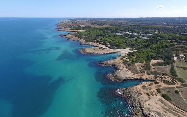 Costa rocciosa con mare turchese e vegetazione mediterranea, vista dall'alto.