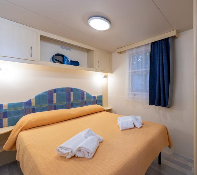 Camera accogliente con letto matrimoniale, asciugamani e finestra con tende blu.