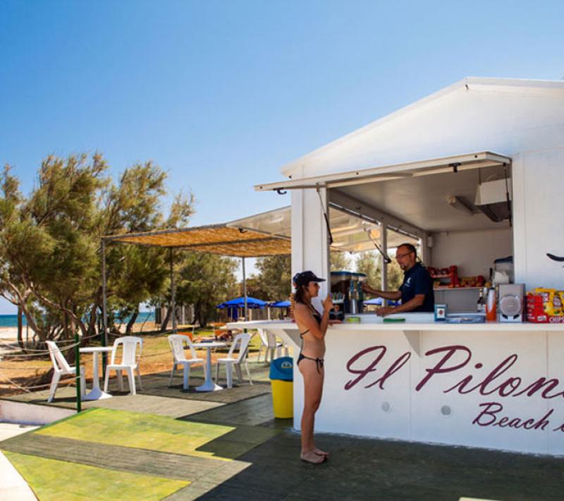 Chiosco sulla spiaggia con cliente, ombrelloni e sedie sotto il sole estivo.