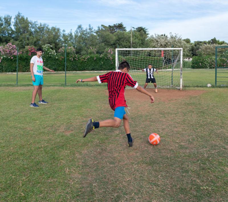 Ragazzi giocano a calcio, uno tira il pallone verso la porta con il portiere.