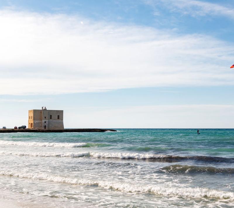 Mare con torre costiera, kitesurfer e cielo sereno.