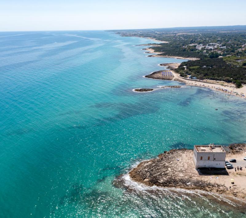 Spiaggia con mare cristallino e torre costiera, vista dall'alto.