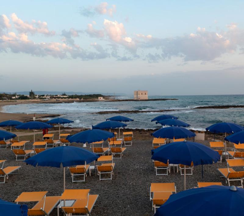 Spiaggia con ombrelloni blu e lettini gialli, mare calmo e cielo sereno.