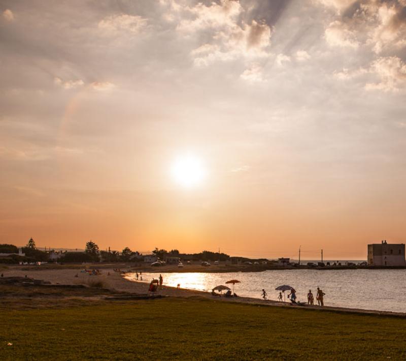 Spiaggia al tramonto con persone e torre sullo sfondo.